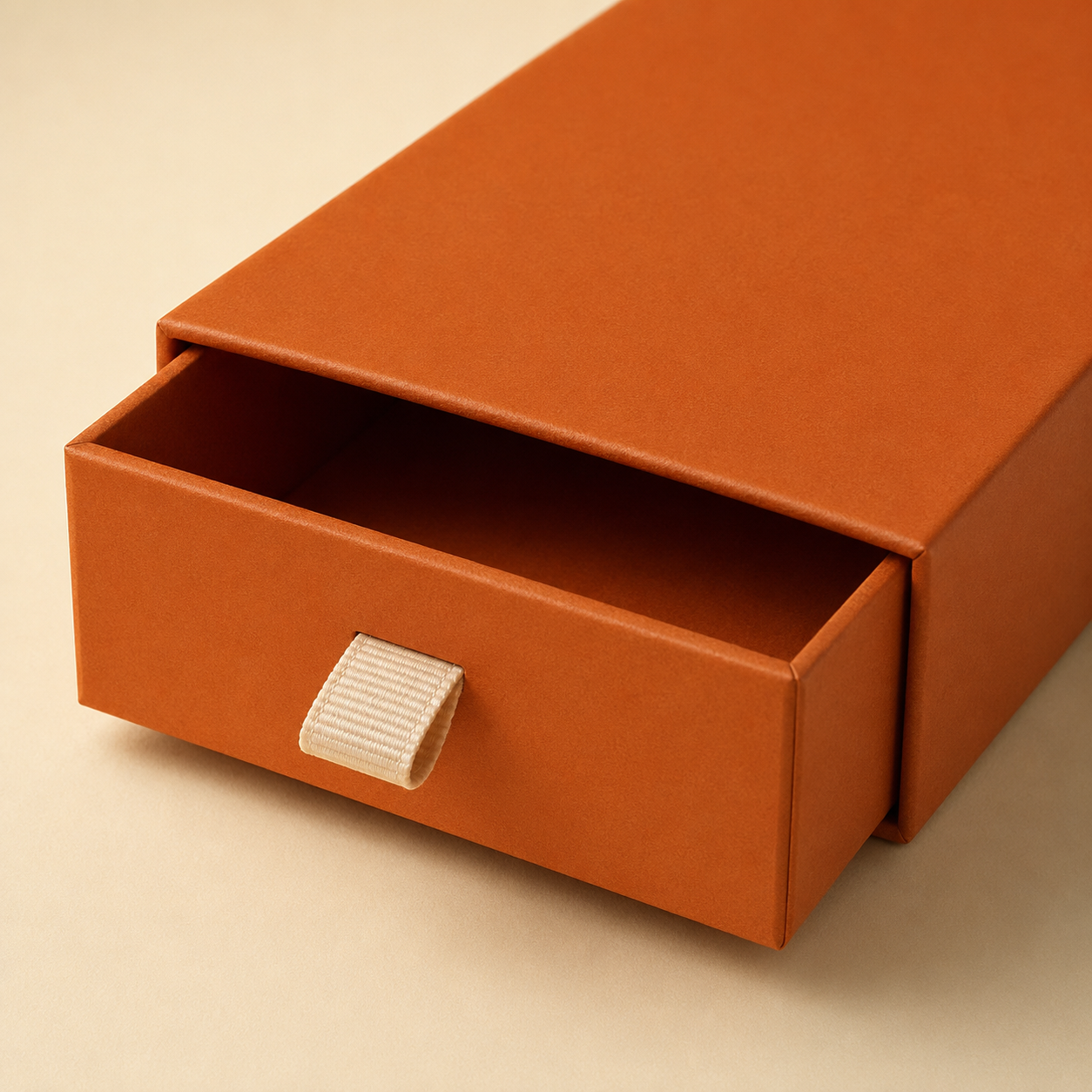 Drawer-style rigid box with a cream ribbon pull tab.