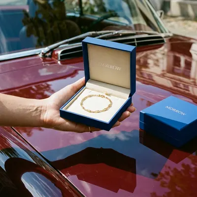 Custom bracelet box in navy blue with cream interior lining, "Morrow" debossed lid, shown open with a gold chain bracelet inside, closed box beside it.