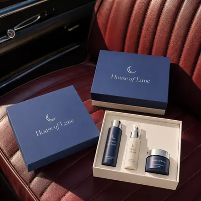 Custom cosmetic rigid boxes in navy blue with silver foil "House of Lune" branding and cream interior insert, shown closed and open with skincare bottles and a jar inside.