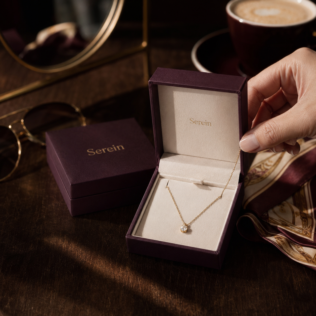 Custom necklace box in deep maroon suede-textured finish with gold foil "Serein" branding and cream interior, shown open with a pendant necklace inside, closed box beside it.