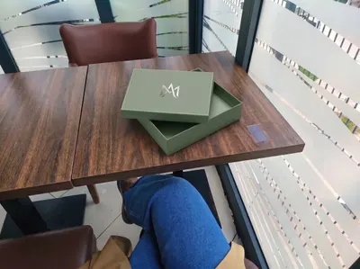 Custom two-piece box in sage green with metallic emblem, shown with lid separated from base on a table.