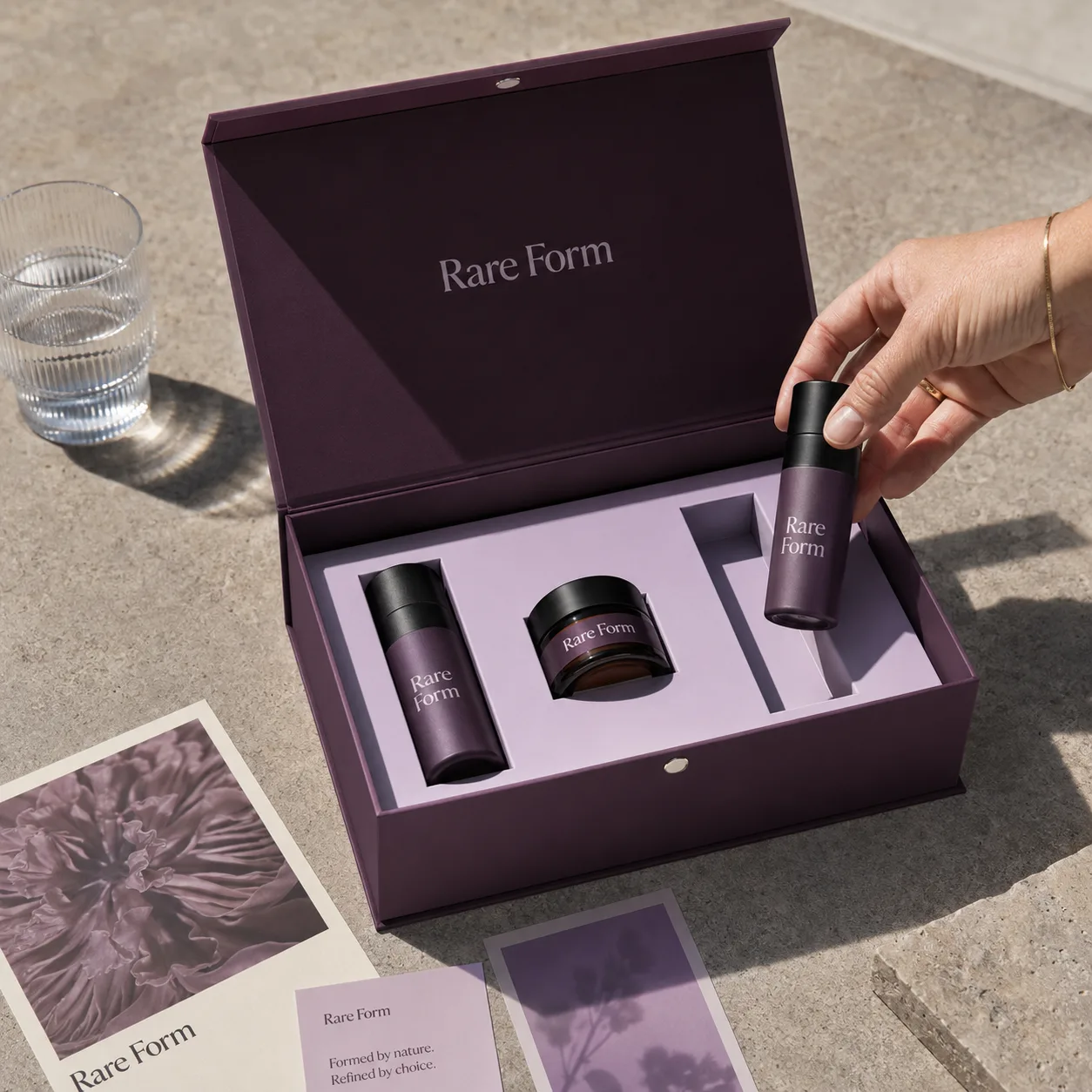 Flip top rigid box in deep plum, magnetic closure, shown open with a fitted insert holding two tube containers and a jar.