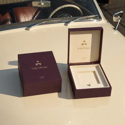 Hinged rigid box in deep plum, shown closed and open on its hinge with a cream velvet tray insert and cutout compartment.