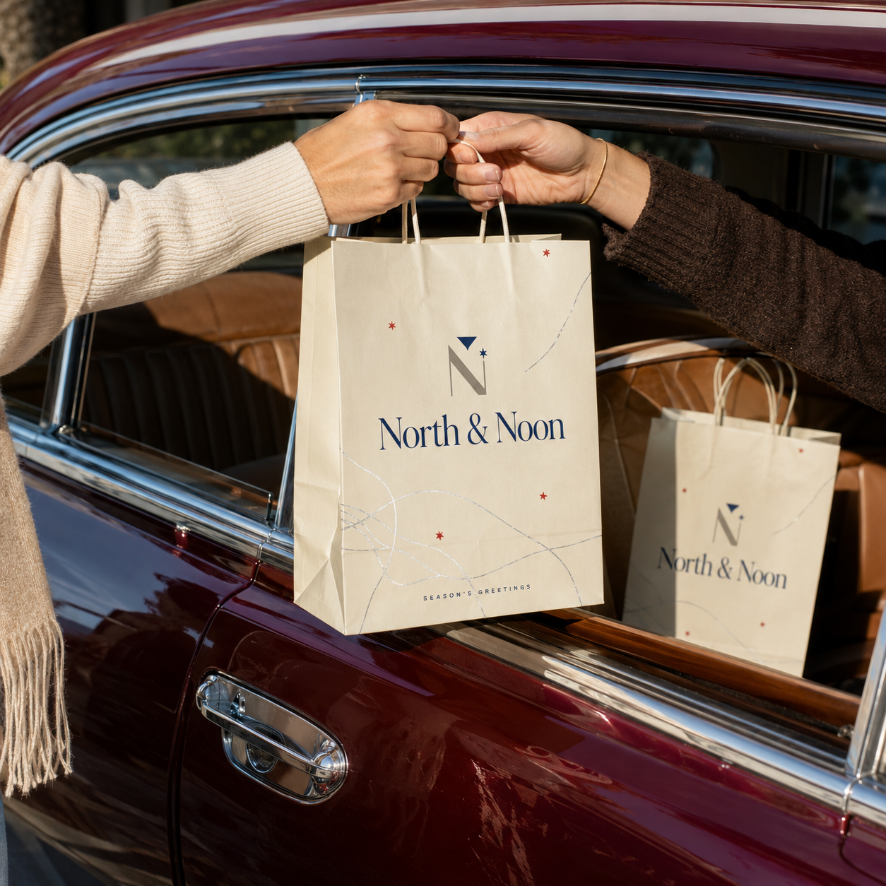 Holiday paper bag in cream kraft with twisted rope handles and a festive star pattern, exchanged through a car window with a matching bag visible behind.