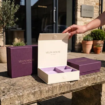 Magnetic closure gift boxes in cream and purple, shown open with a flip-top lid revealing a compartmented interior tray.