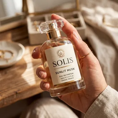 Perfume label on a glass spray bottle, held in hand, showing a printed design on the front panel.