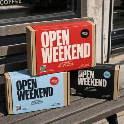 Promotional packaging boxes in red, blue, and black with a QR code, shown closed and stacked on an outdoor bench.