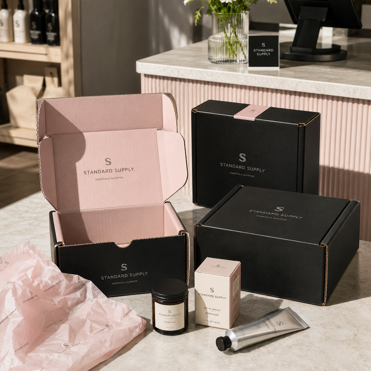 Roll end tuck top boxes in black with a pink interior, shown open and closed alongside jewelry-brand contents on a retail counter.